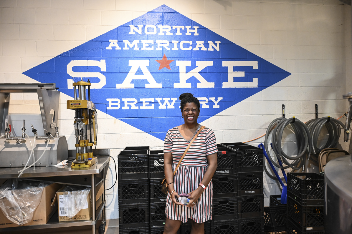 Woman smiling besides Sake brewing equipment.